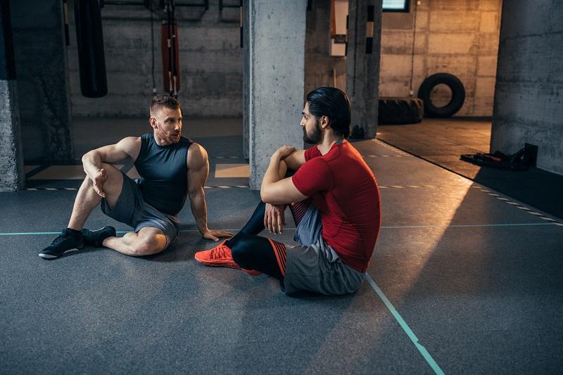 Dwaj muskularni mężczyźni siedzą na podłodze na siłowni